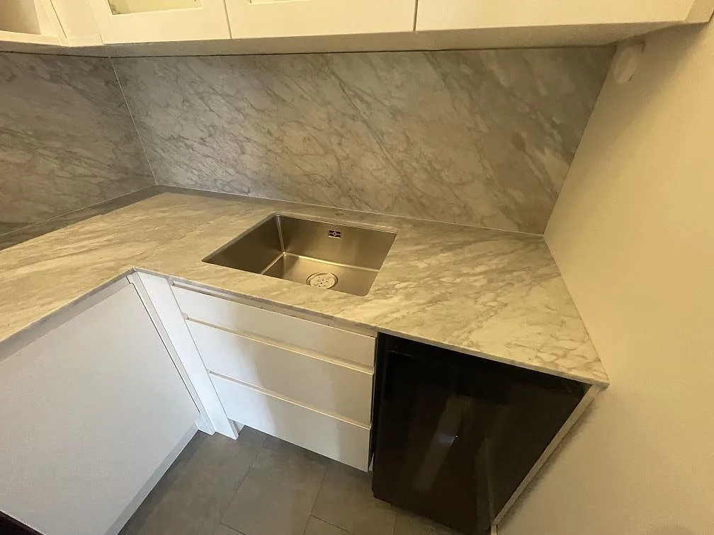 Diskbänksdel i matt Carrara C marmor i Örebro med synlig diskho, ådrad bänkyta och stänkskydd i samma sten.