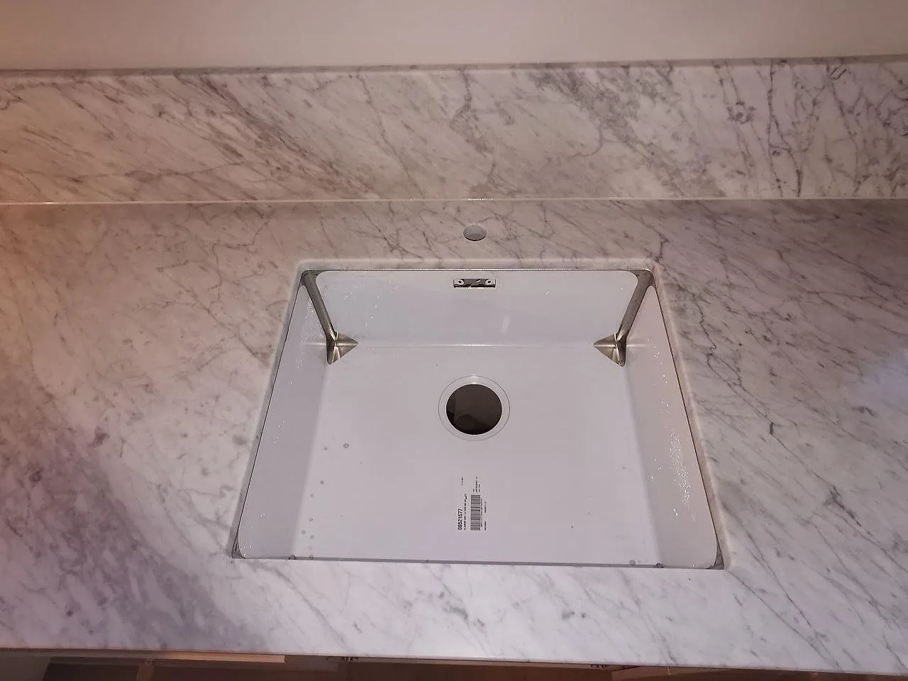 Underlimmad vit Blanco Claron-diskho i en matt köksbänkskiva av Carrara CD-marmor i ett kök i Ramlösa.