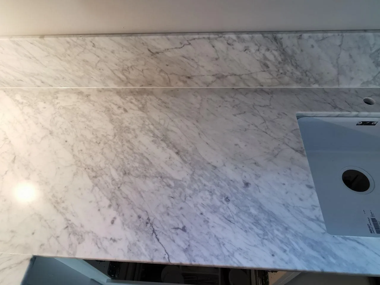 Matt köksbänkskiva i Carrara CD-marmor med tydlig grå ådring och uppvikt stänkskydd i ett kök i Ramlösa.
