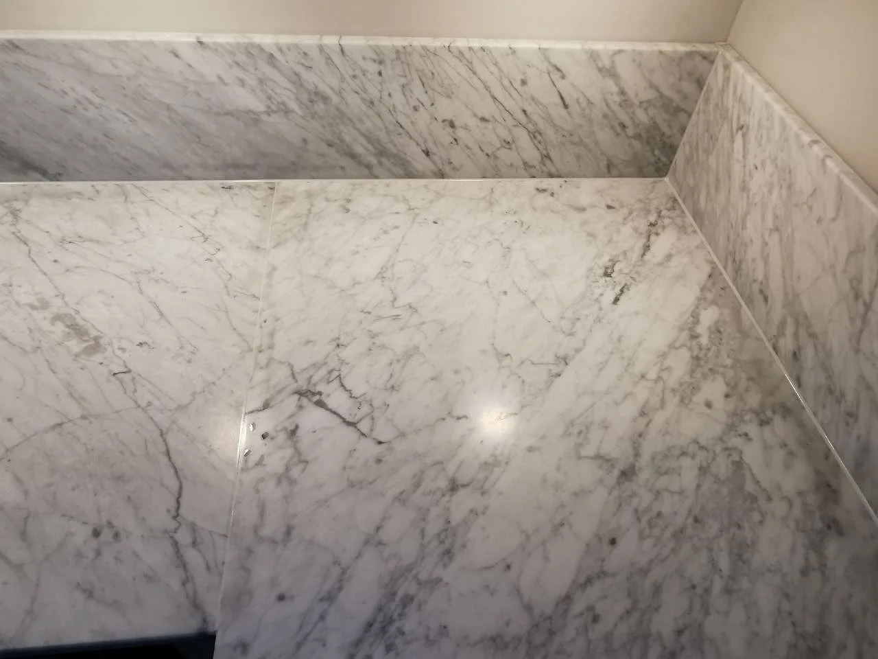 Hörnparti av matt Carrara CD-marmor med uppvikt stänkskydd i samma marmor, där den grå ådringen löper genom köksbänken i Ramlösa.