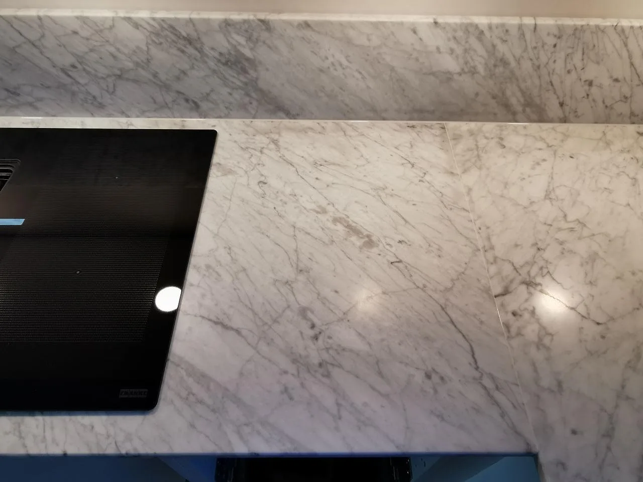 Övermonterad svart induktionshäll från Franke på en matt köksbänk i Carrara CD-marmor med uppvikt stänkskydd i Ramlösa.