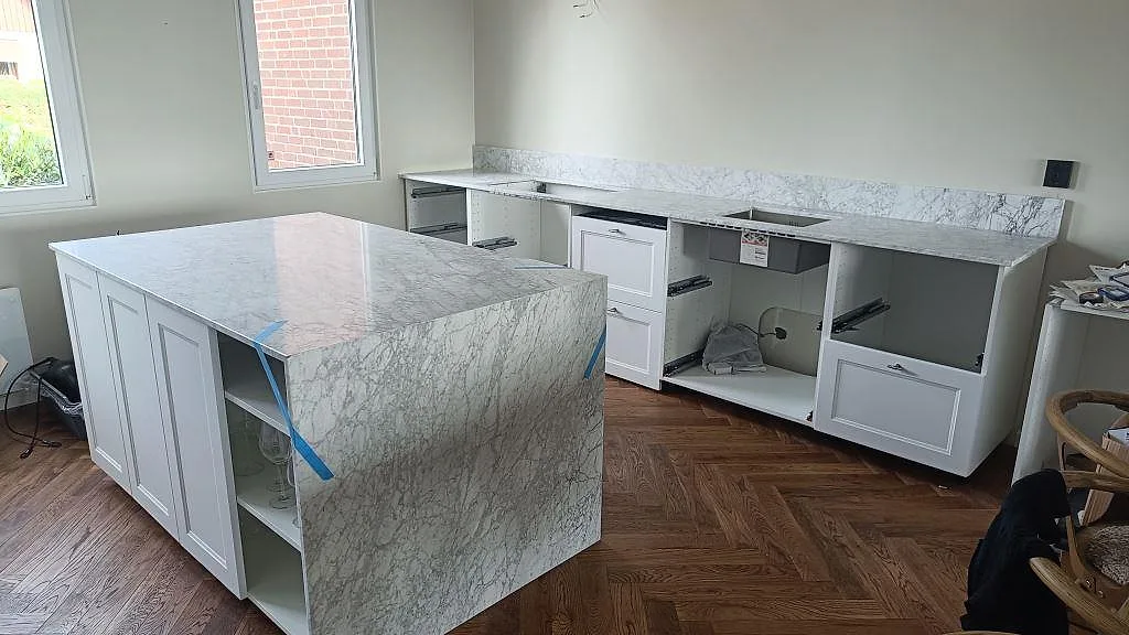 Köksbänkskiva i Carrara C marmor, matt, med stor köksö, väggbänk och stänkskydd under montering i Ramlösa.