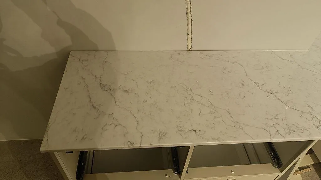 Närbild på polerad Carrara C marmorbänkskiva med grå ådring över öppna köksstommar i Rydebäck.