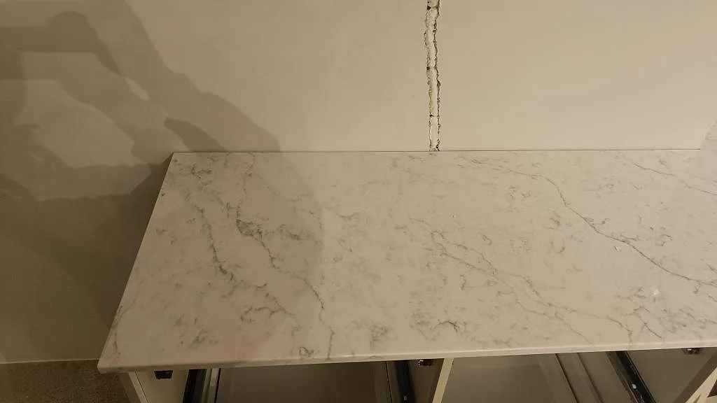 Detalj av polerad Carrara C marmor som installerad köksbänkskiva mot vägg under montering i Rydebäck.