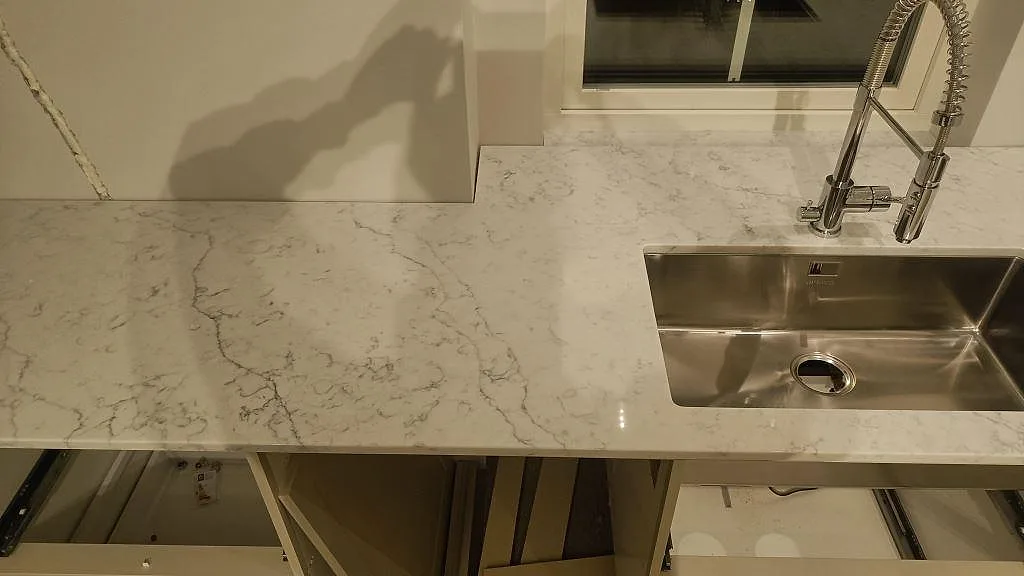 Köksbänkskiva i polerad Carrara C marmor med rostfri diskho och grå ådring över öppna stommar i Rydebäck.