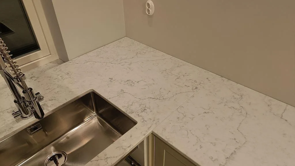 Hörnparti av polerad Carrara C marmorbänkskiva med rostfri diskho och ljus grå ådring i Rydebäck.