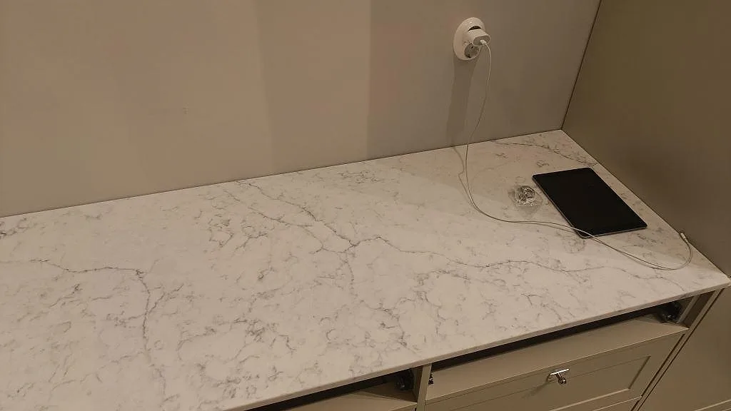 Lång arbetsyta i polerad Carrara C marmorbänkskiva med grå ådring och eluttag på väggen i Rydebäck.