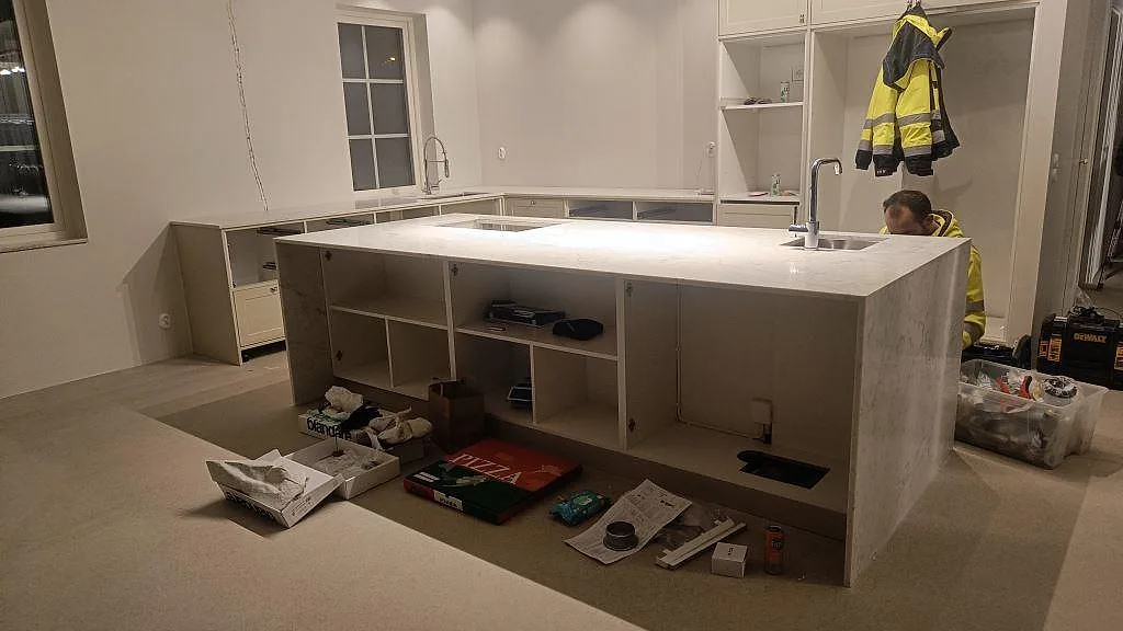 Köksbänkskiva och stor köksö i Carrara CD marmor, polerad, i ett kök under montering i Rydebäck.