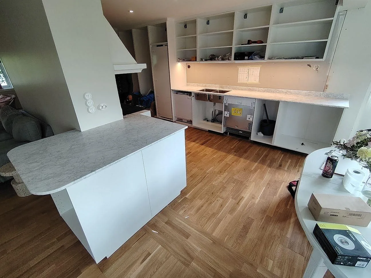 Kök i Saltsjö Boo under montering med matt Carrara C marmor på halvö och lång bänkskiva längs väggen.