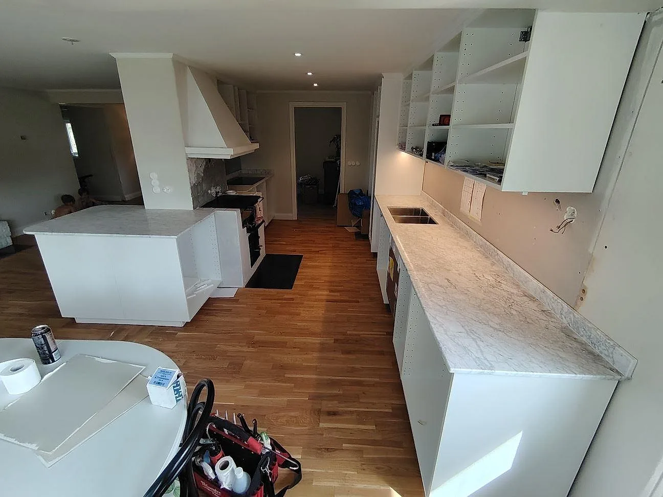 Lång köksbänkskiva i matt Carrara C marmor med diskho, stänkkant och halvö i ett kök under montering i Saltsjö Boo.