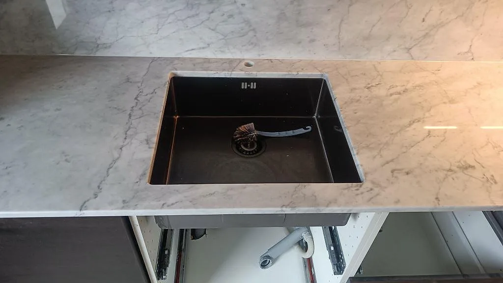 Närbild på underlimmad svart diskho i en polerad Carrara C köksbänkskiva med öppen stomme i Skee.