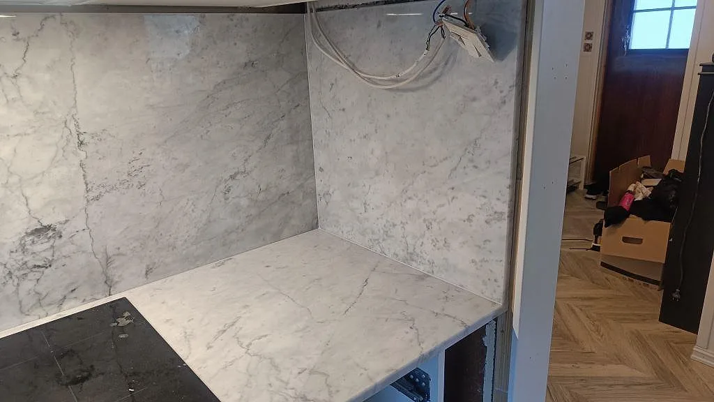 Hörnvy av Carrara C marmor med hög stänkvägg, polerad köksbänkskiva och synlig montering i Skee.
