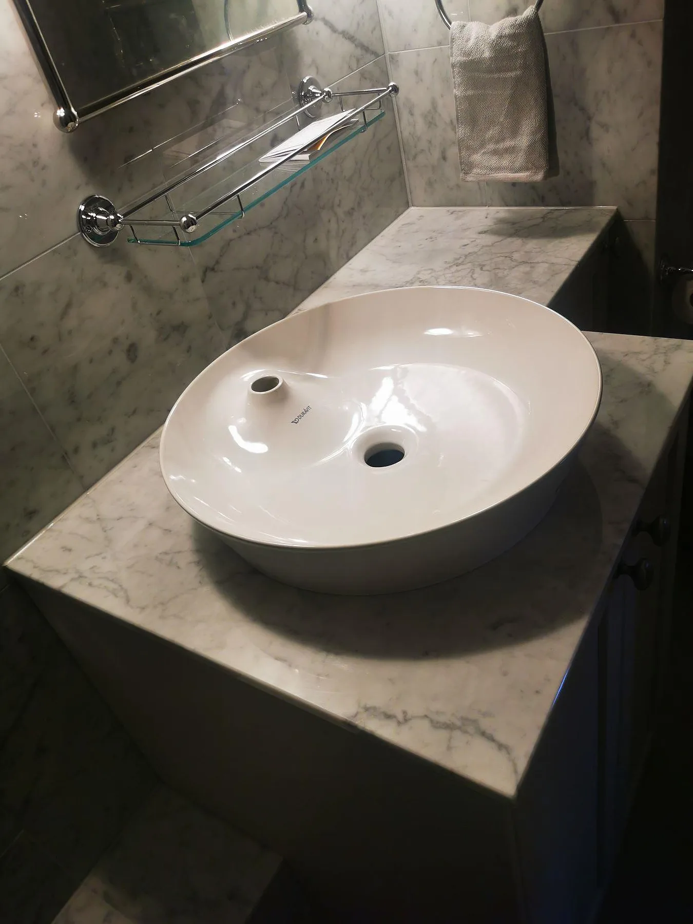 Bänkskiva i vit Carrara C-marmor, polerad, med ovanpåliggande vitt tvättställ i keramik i ett badrum med matchande Carrara-kakel i Stockholm.