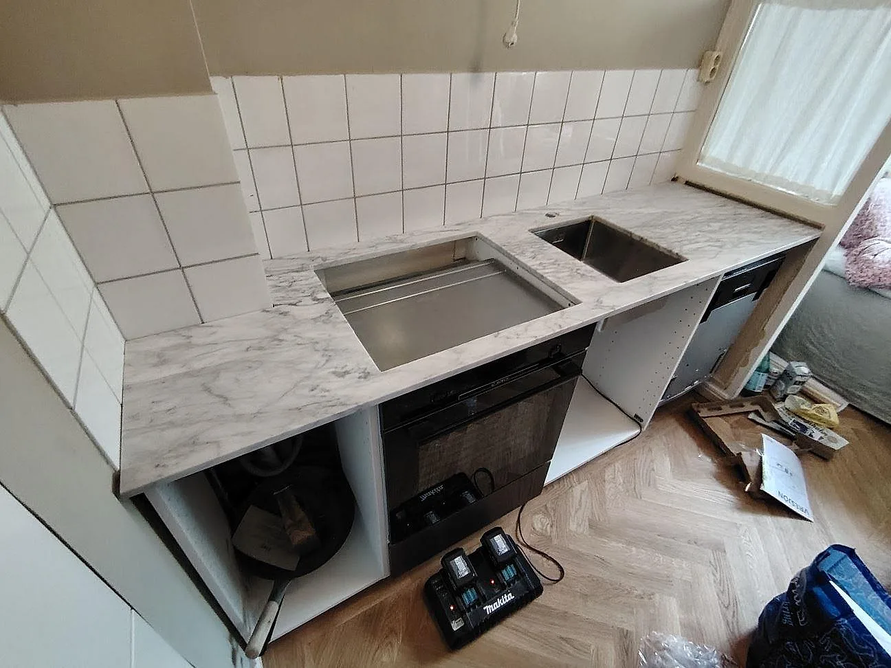 Köksbänkskiva i matt Carrara C marmor, 20 mm, med underlimmad rostfri diskho och hällöppning mot vitt kvadratiskt kakel i Stockholm.