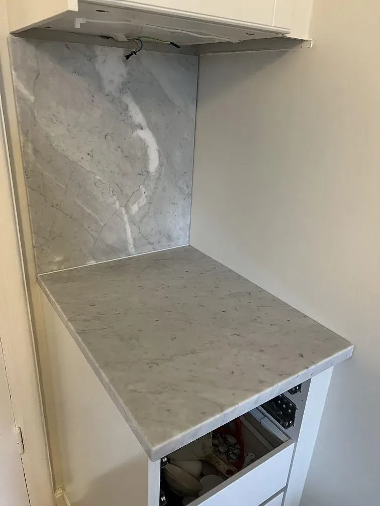 Polerad Carrara C marmor som bänkskiva och väggskiva i en smal köksnisch under montering i Stockholm.