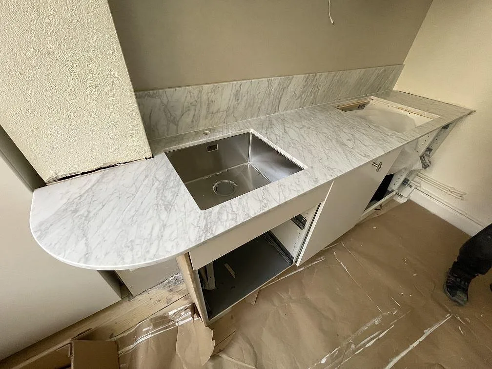 Köksbänkskiva i matt Carrara C marmor med rundad avslutning, synlig diskho och stänkkant i ett kök i Stockholm.