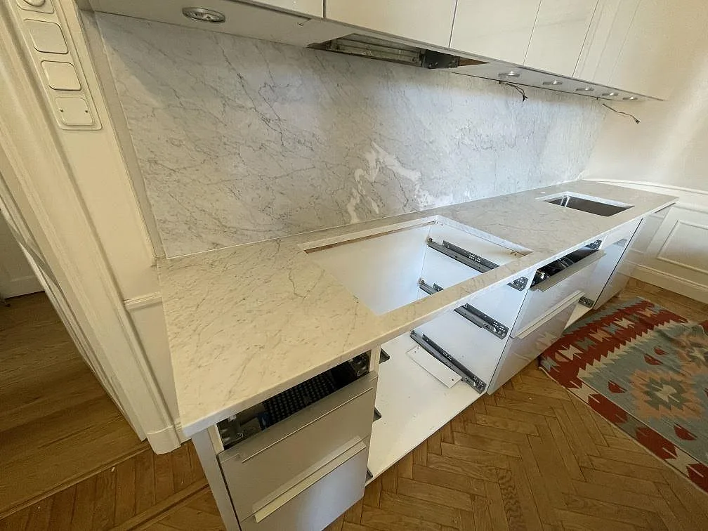 Matt Carrara C marmor sedd från hälluttaget, med bänkskiva, diskho och stenpanel i ett kök i Stockholm.