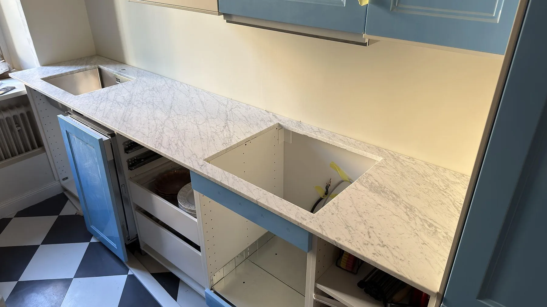 Installerad köksbänkskiva i matt Carrara C, marmor, med diskho, större urtag och blå skåpsdelar i Stockholm.