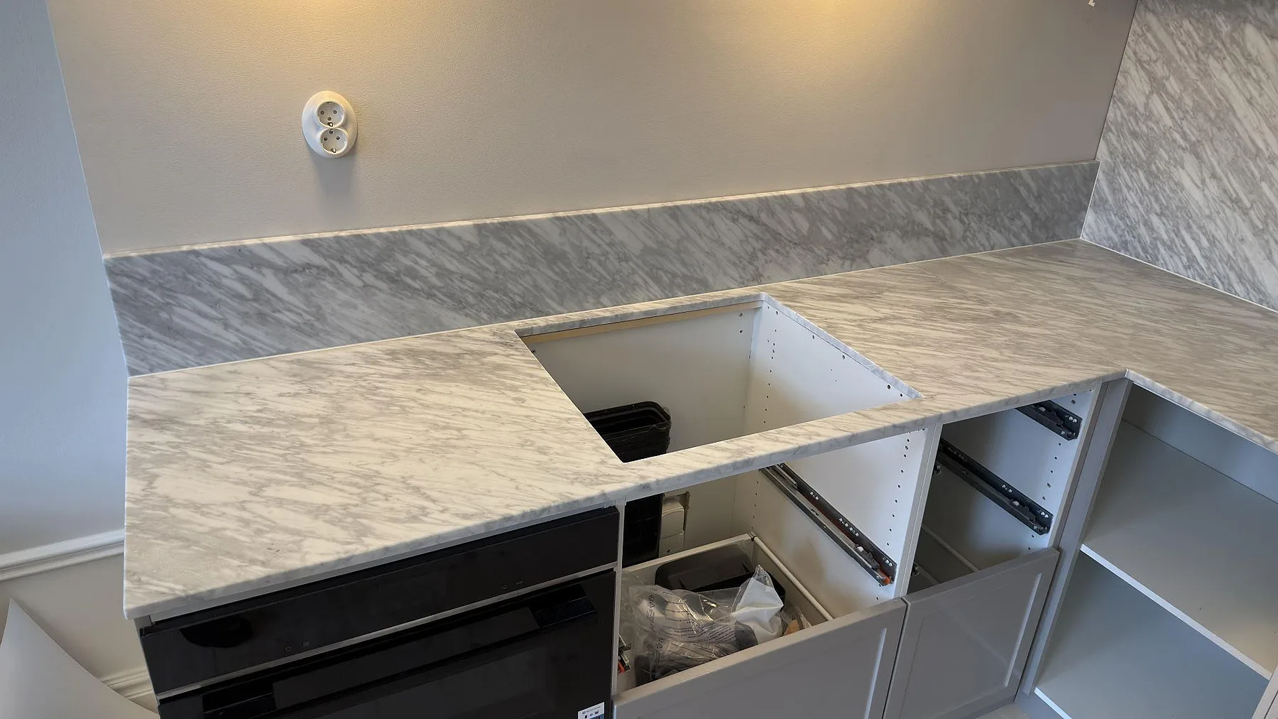 Närbild av matt Carrara C marmorbänkskiva i Stockholm med grå ådring, låg stänkkant och öppning för häll i ett kök under montering.