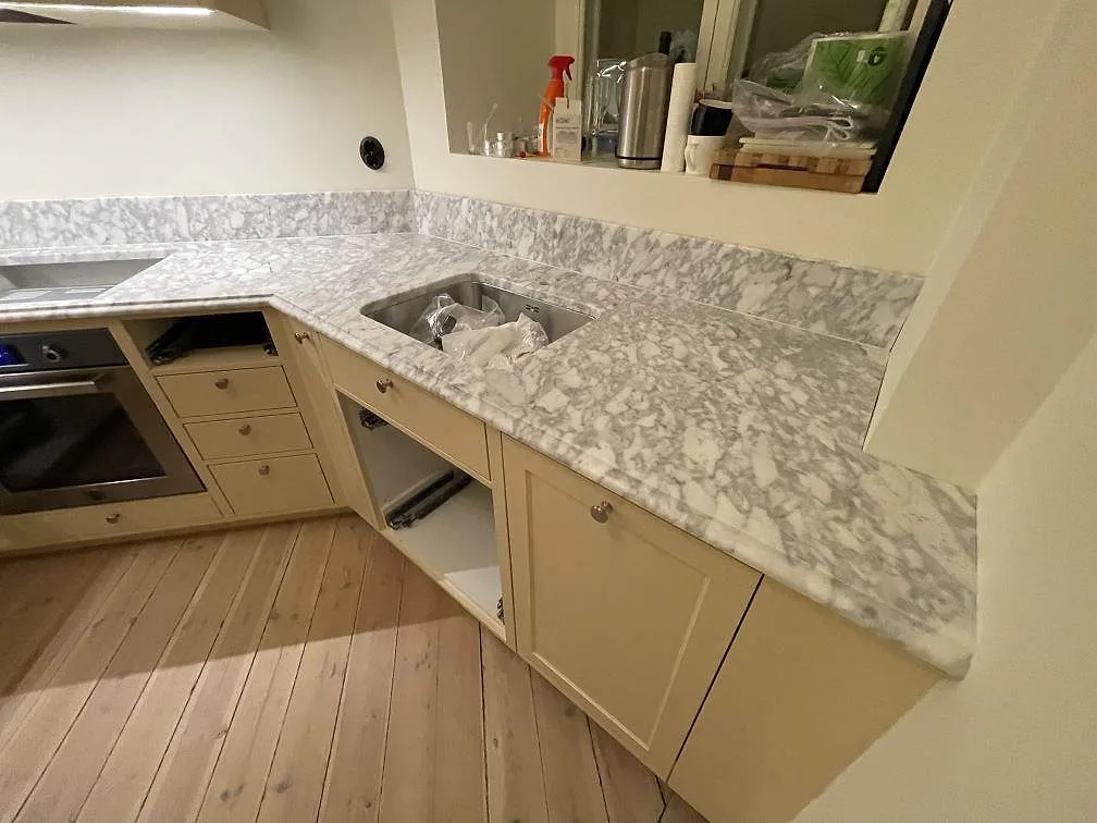 Diskzon i Stockholm med matt Carrara C marmorbänkskiva i marmor, synlig diskho och uppvikt stänkkant under köksmontering.