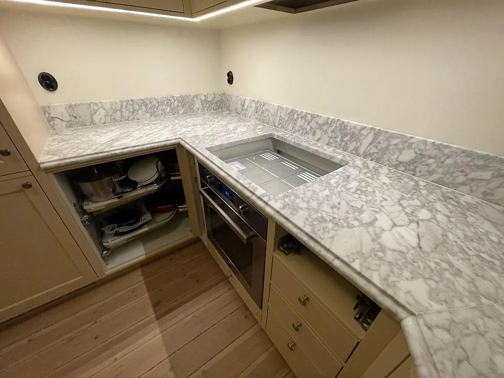 Närbild på matt Carrara C marmorbänkskiva i marmor med grå ådring, uppvikt stänkkant och hällöppning i ett kök i Stockholm.