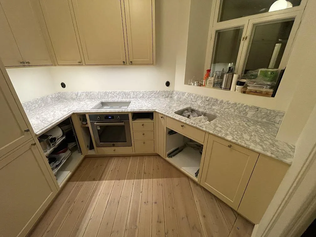 U-format kök i Stockholm med matt Carrara C marmorbänkskiva i marmor, uppvikt stänkkant, spisdel och diskzon under montering.