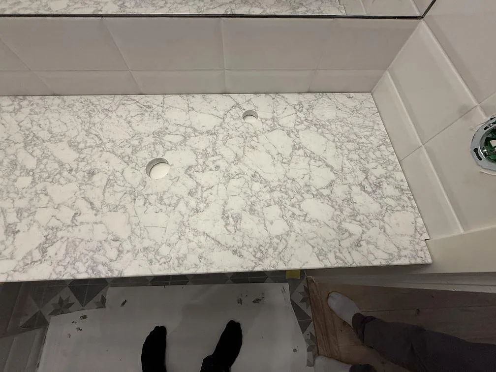Närbild på matt Carrara C marmorskiva i badrum i Stockholm, med grå ådring och runda urtag.