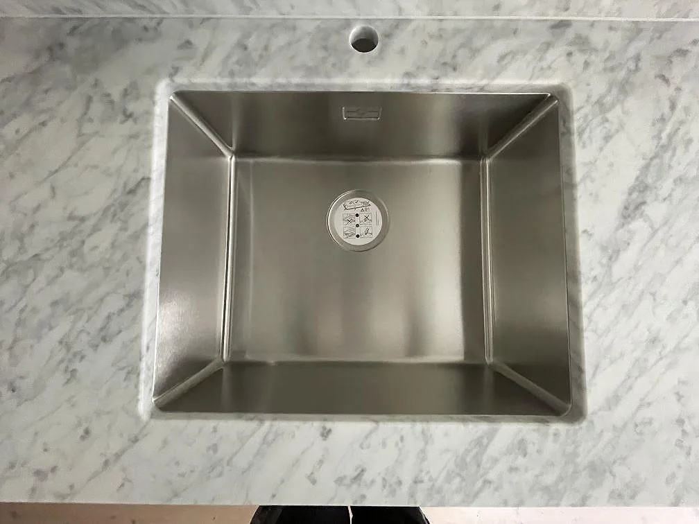 Närbild på Carrara CD-marmorns gråa ådring med en underlimmad rostfri diskho och kranhål i ett kök i Stockholm.