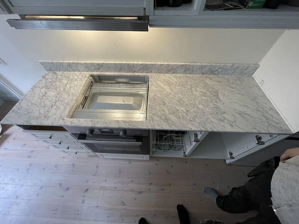 Köksbänkskiva i Carrara CD-marmor i Stockholm med urtag för inbyggda vitvaror och öppna köksstommar under montering.
