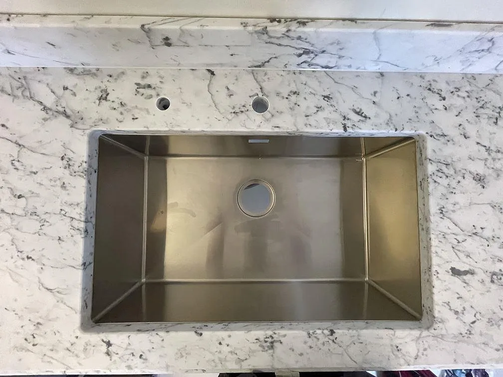 Underlimmad rostfri diskho med två kranhål i en köksbänkskiva av matt Carrara C marmor i ett kök i Stockholm.