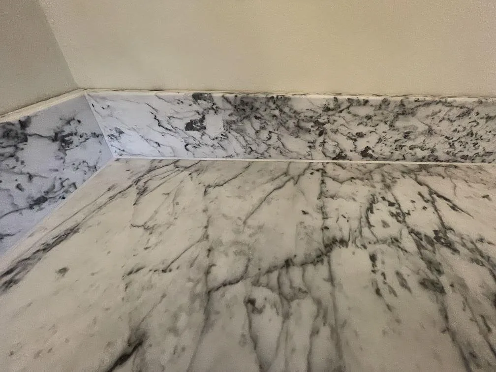 Hörn av köksbänkskiva i matt Carrara C marmor med uppvikt stänkkant i samma sten i ett kök i Stockholm.