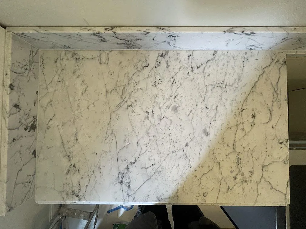 Köksö i Carrara C marmor med matt yta och kraftig grågrön ådring, sedd ovanifrån under montering i ett kök i Stockholm.
