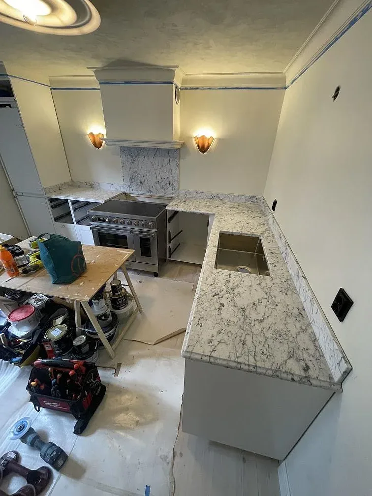 Köksbänkskiva och köksö i vit Carrara C marmor med matt yta under montering i ett kök i Stockholm, med fristående rostfri spis och tydlig grå ådring.