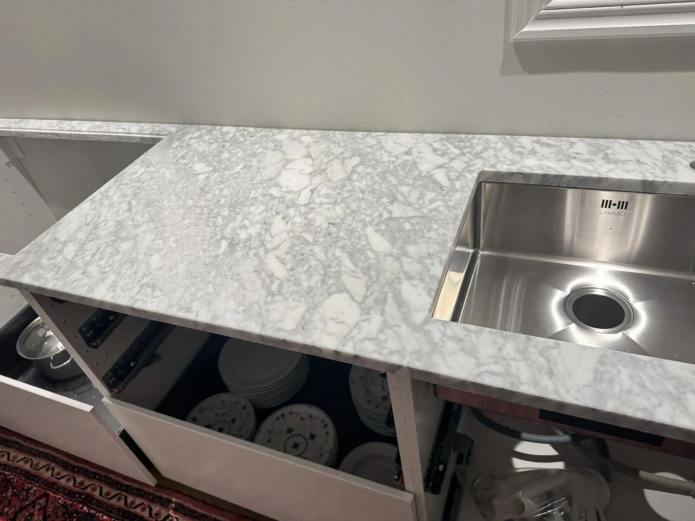 Carrara C marmorbänkskiva, matt, med rostfri diskho och öppna köksstommar under montering i Stora höga.