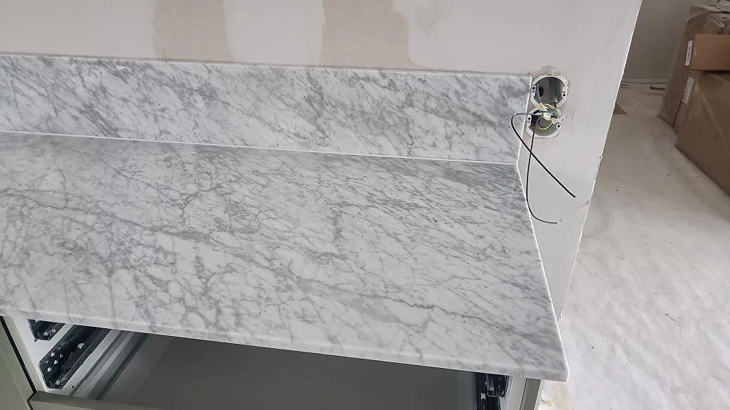 Detalj av 20 mm Carrara C bänkskiva med stänkkant, marmorerad yta och öppna gröna köksstommar i Svanshall.