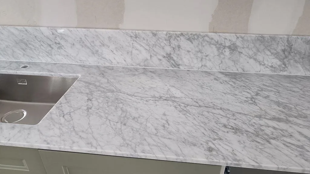Carrara C köksbänkskiva med rostfri diskho, grå marmorådring och uppvikt stänkkant under montering i Svanshall.