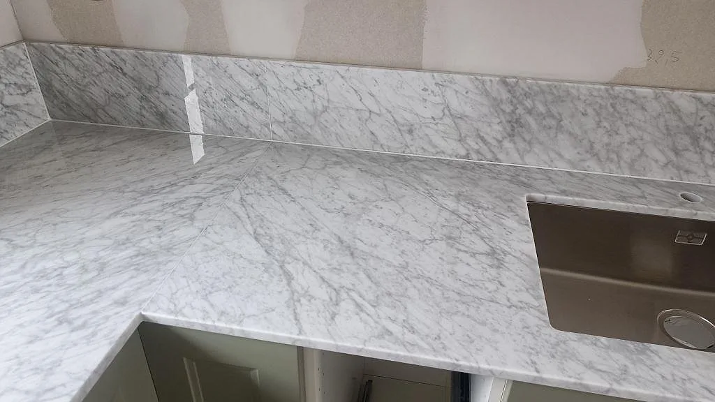 Närbild av Carrara C marmor runt underlimmad rostfri diskho, med L-format hörn och stänkkant i kök i Svanshall.