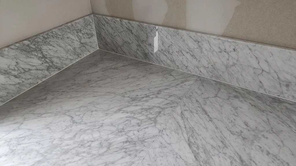 Hörnsektion av Carrara C marmorbänkskiva med uppvikt stänkkant och tydliga grå vener i Svanshall.