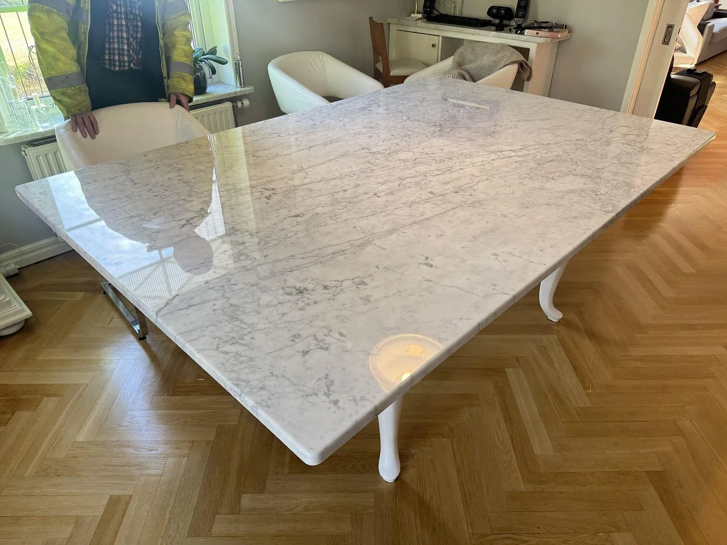 Stor bordsskiva i 30 mm Carrara C marmor, polerad, fotograferad från sidan med parkettgolv och matplats i Svenshögen.