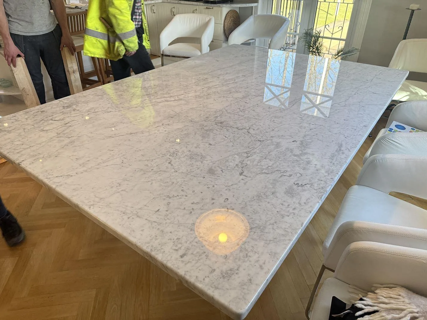 Polerad Carrara C marmor som bordsskiva på vita bordsben, med fönsterspeglingar över den blanka ytan i Svenshögen.