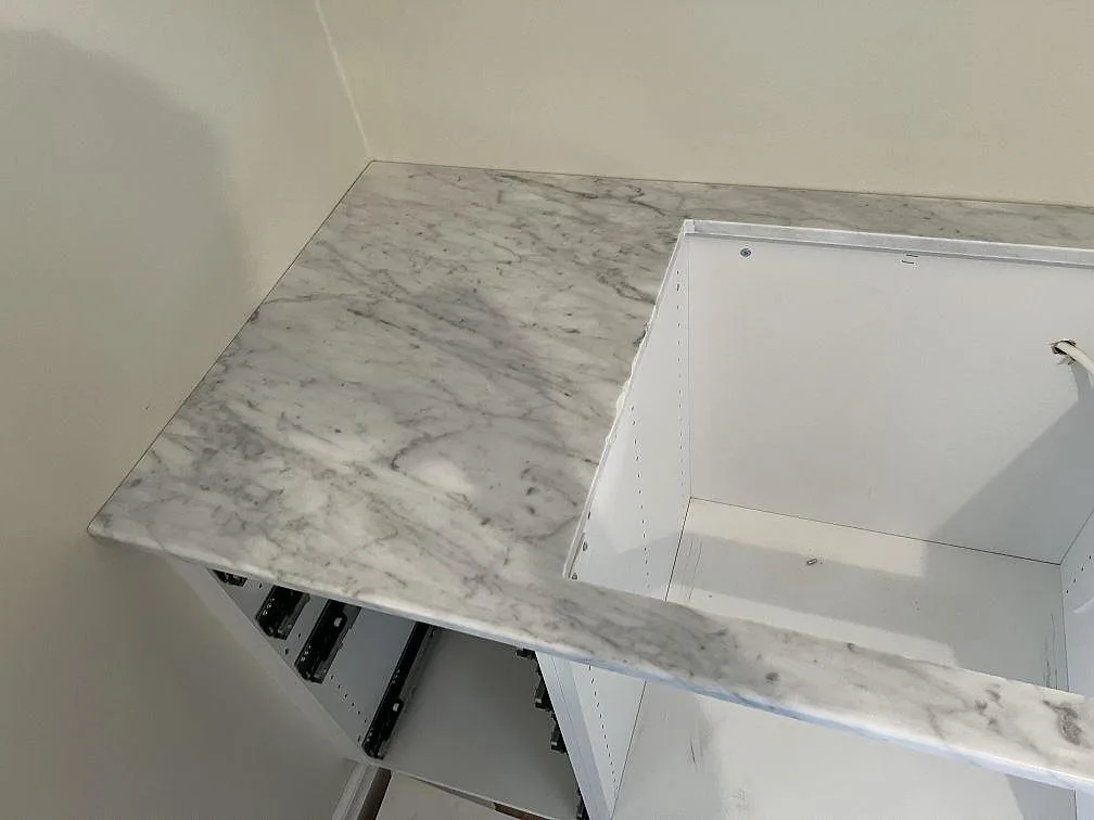 Närbild av polerad Carrara C marmor runt ett rektangulärt urtag på vita köksstommar i Trollhättan.