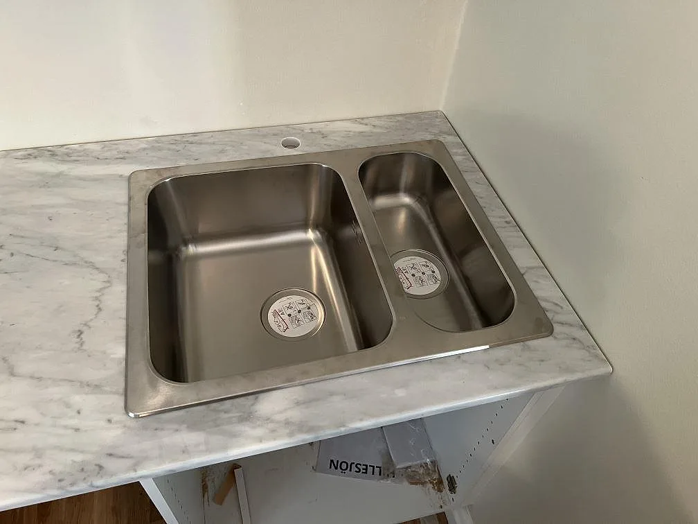 Diskbänksdel i polerad Carrara C marmor med övermonterad rostfri dubbelho och ljusa väggar i Trollhättan.