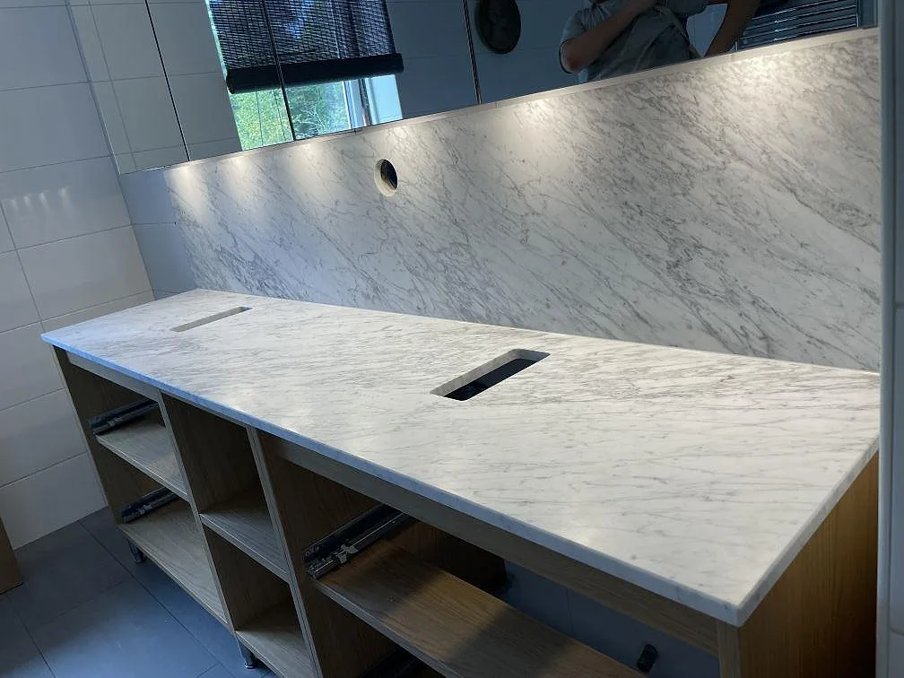 Närbild av Carrara C marmor, matt 20 mm, som badrumsbänkskiva med väggbeklädnad och öppna trästommar i Vaxholm.