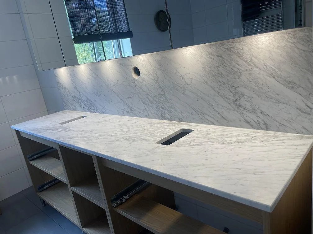 Matt Carrara C marmorbänkskiva i badrum i Vaxholm, med två rektangulära urtag och hög väggskiva under spegeln.