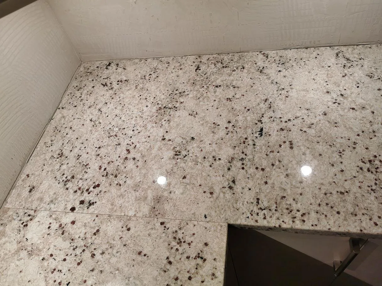 Svart induktionshäll monterad ovanpå en polerad Colonial White granitbänkskiva i ett kök i Lomma.