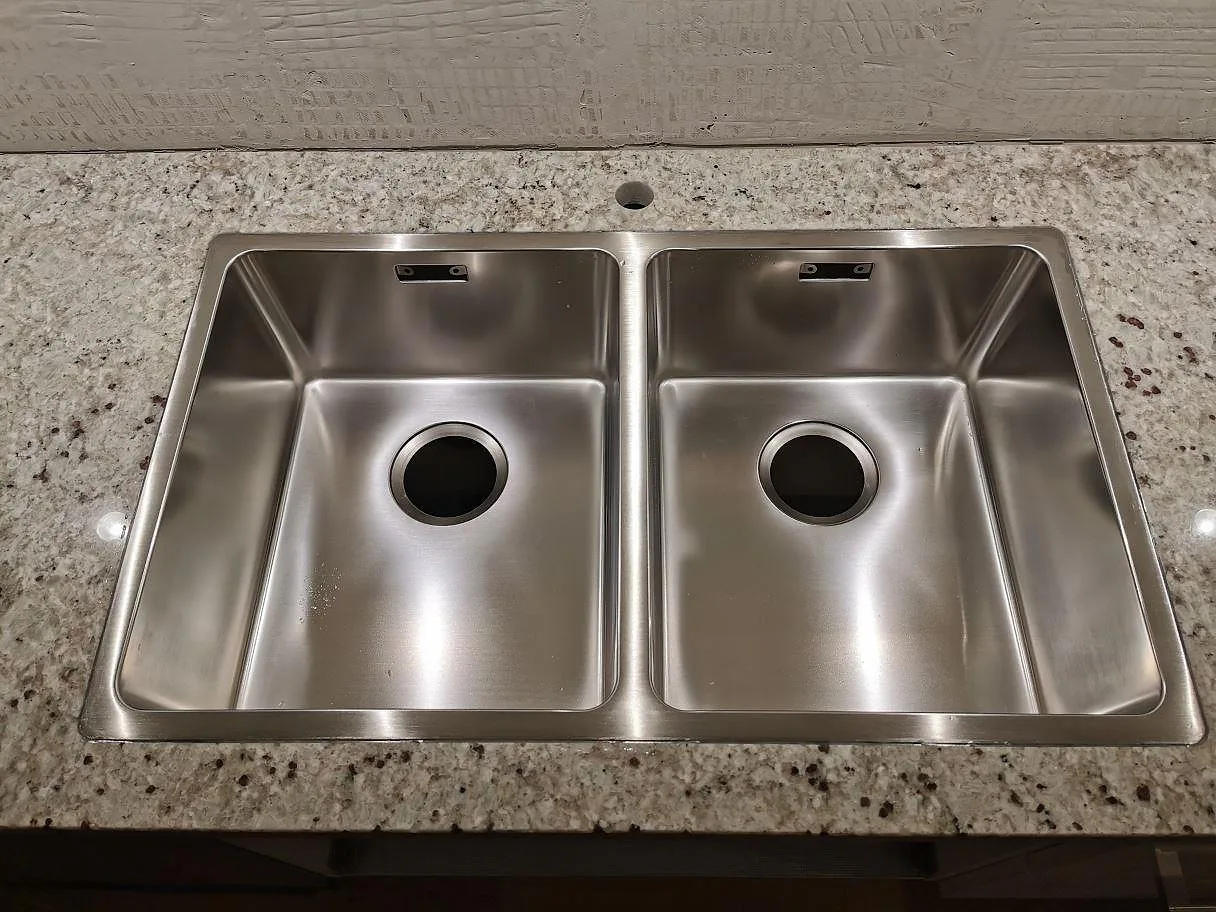 Rostfri diskho monterad i nivå med polerad Colonial White granit, närbild på den gräddvita spräckliga stenytan i ett kök i Lomma.
