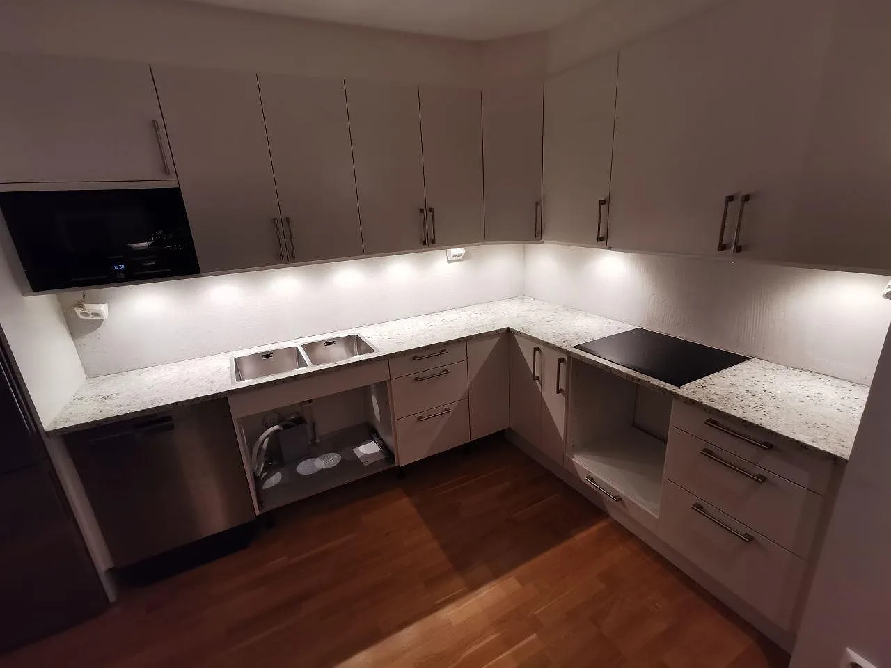 Köksbänkskiva i ljus Colonial White granit, polerad, i ett vinkelkök i Lomma med dubbel rostfri diskho och induktionshäll.
