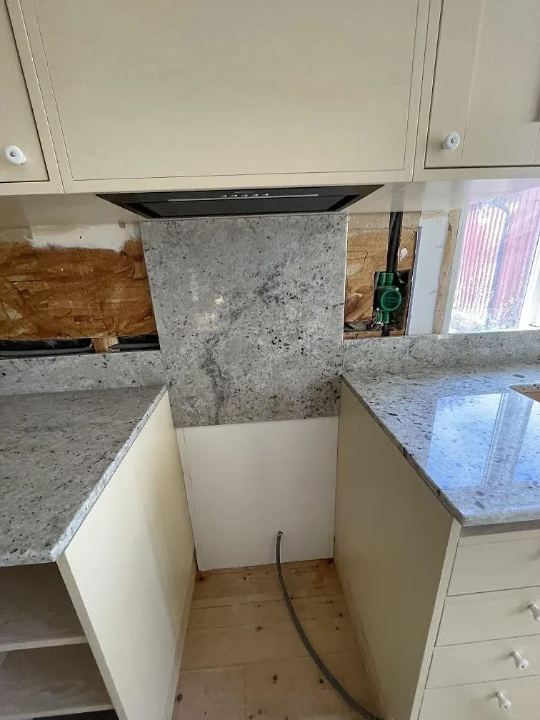 Hörnparti av polerad Colonial White-granit med uppvikt stänkkant och öppna stommar i ett kök under montering i Östra Sönnarslöv.