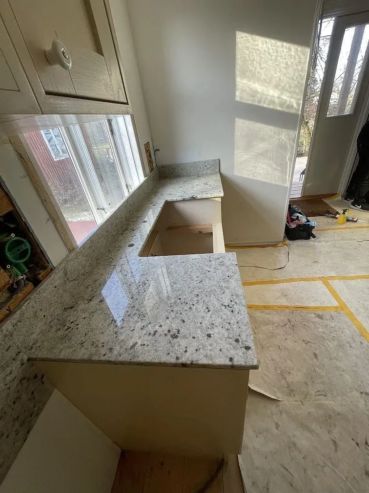 Köksbänkskiva i Colonial White-granit med underlimmad diskhoplats framför fönstret i ett kök i Östra Sönnarslöv.