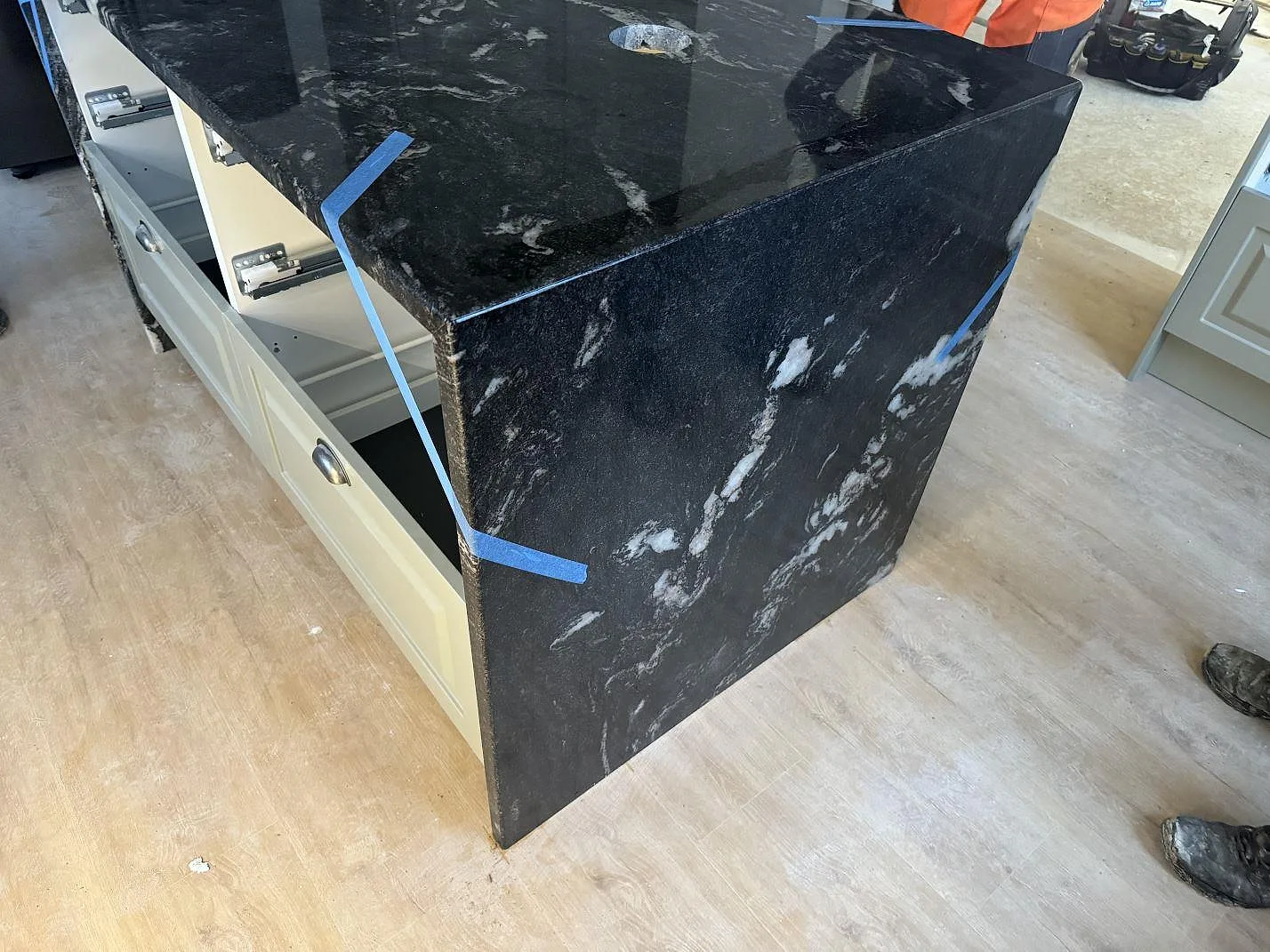 Vattenfallsgavel och blank ovansida i Cosmic Black granit på en köksö under montering i Älmhult.